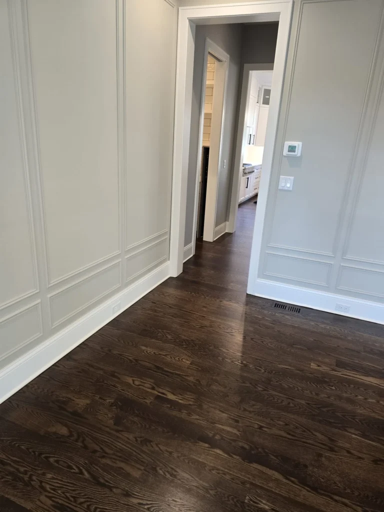 Refinished dark hardwood flooring in dining room with white wall molding