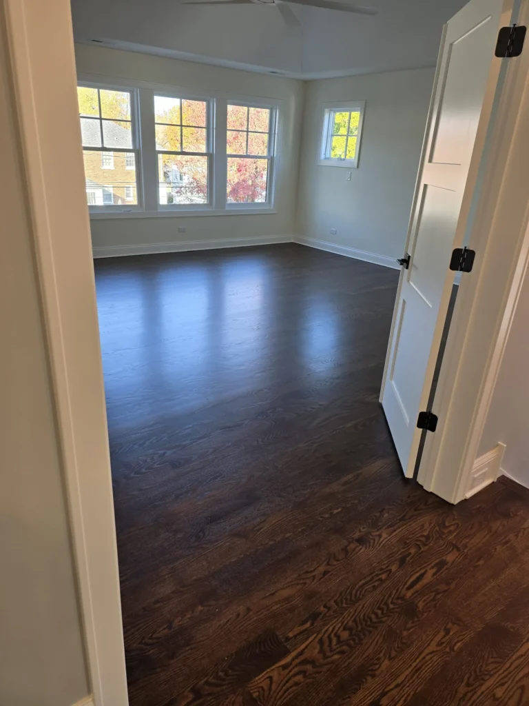 Dark stained hardwood flooring refinished in bright bedroom